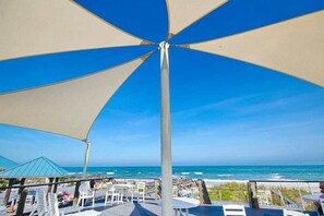 A beachside patio with a large umbrella, outdoor seating, and a view of the ocean. - Seaside Sanctuary at Litchfield by the Sea (Pawleys Island)