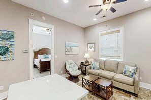 A well-lit room with a bed, a chair, a sofa, a table, and a ceiling fan. - North Beach Villas 201 (North Myrtle Beach)
