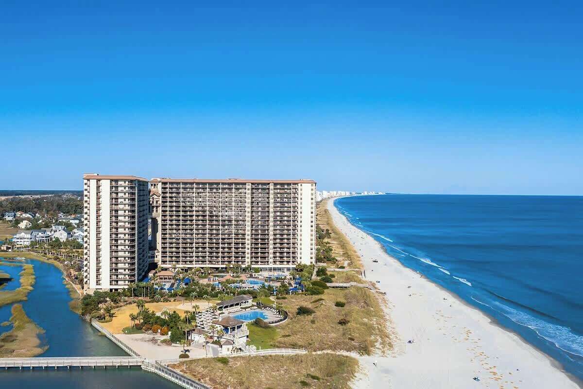 A high-rise hotel with multiple floors, a beach, and a body of water.