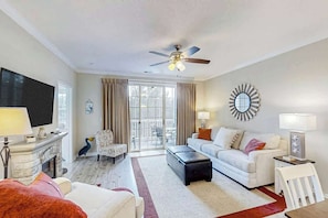 A living room with a flat-screen TV, a ceiling fan, a fireplace, a sofa, a coffee table, and a dining area with a table and chairs. - Barefoot Landing Beach and Golf  Resort Villa (North Myrtle Beach)