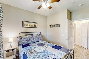 Ein Schlafzimmer mit Bett, Deckenventilator, Nachttischlampe, einem gerahmten Bild an der Wand und einer Tür.