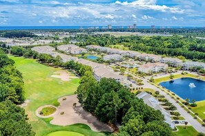 Ein Golfplatz mit Clubhaus, Parkplatz und einem Gewässer.