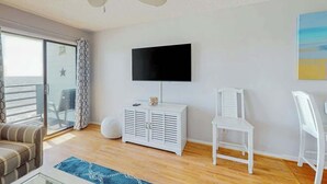 A room with a television mounted on the wall, a white cabinet, a ceiling fan, a sofa, and a chair. - Paradise Palms Retreat (Murrells Inlet)