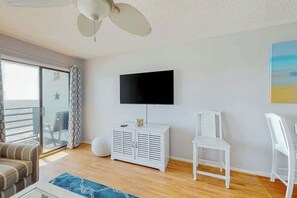 Ein Zimmer mit an der Wand montiertem Fernseher, einem weißen Schrank, einem Deckenventilator, einer Couch und einem Sessel.