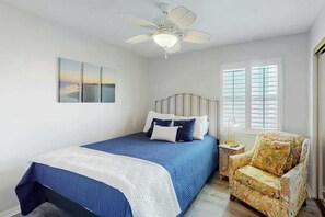 A bedroom with a bed, a chair, a ceiling fan, a window with blinds, and a painting on the wall. - Paradise Palms Retreat (Murrells Inlet)