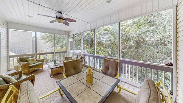 A sunroom with a table and chairs, large windows, and a ceiling fan. - A Shore Pleasure Retreat (North Myrtle Beach)
