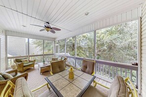 Uma sala de sol com mesa e cadeiras, janelas amplas e um ventilador de teto.