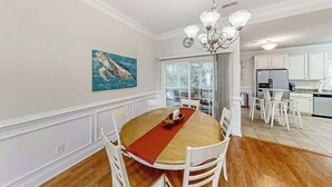 A dining area with a round table, white chairs, a red runner, and a chandelier. - A Shore Pleasure Retreat (North Myrtle Beach)
