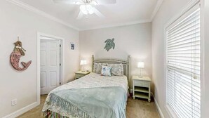 A bedroom with a bed, two bedside tables, a ceiling fan, a door, and a window with blinds. - A Shore Pleasure Retreat (North Myrtle Beach)
