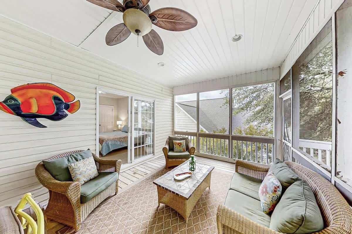 A covered porch with wicker furniture, a ceiling fan, and large windows offering a view of the outdoors.