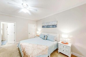 Een slaapkamer met een bed, nachtkastjes, een plafondventilator en een schilderij aan de muur.