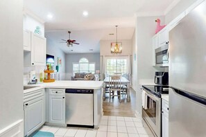 A modern kitchen with white cabinetry, a central island, and a dining area with a chandelier. - Gardens at Cypress Bay 10-302 (Little River)
