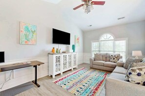 Un salon doté d’un téléviseur à écran plat, d’un meuble blanc, d’un tapis à motifs et d’un ventilateur de plafond.