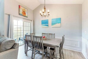 A dining area with a wooden table and chairs, a chandelier, and artwork on the wall. - Gardens at Cypress Bay 10-302 (Little River)