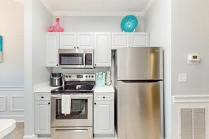 A compact kitchen with white cabinetry, a stainless steel refrigerator, a microwave, and a stove. - Gardens at Cypress Bay 10-302 (Little River)