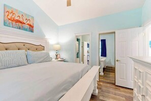 Ein Schlafzimmer mit einem großen Bett, einem Nachttisch mit Lampe, einer Tür zu einem Badezimmer und einem Gemälde an der Wand.