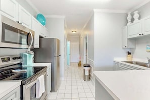 A modern kitchen with stainless steel appliances, white cabinetry, and a tiled floor. - Gardens at Cypress Bay 10-302 (Little River)