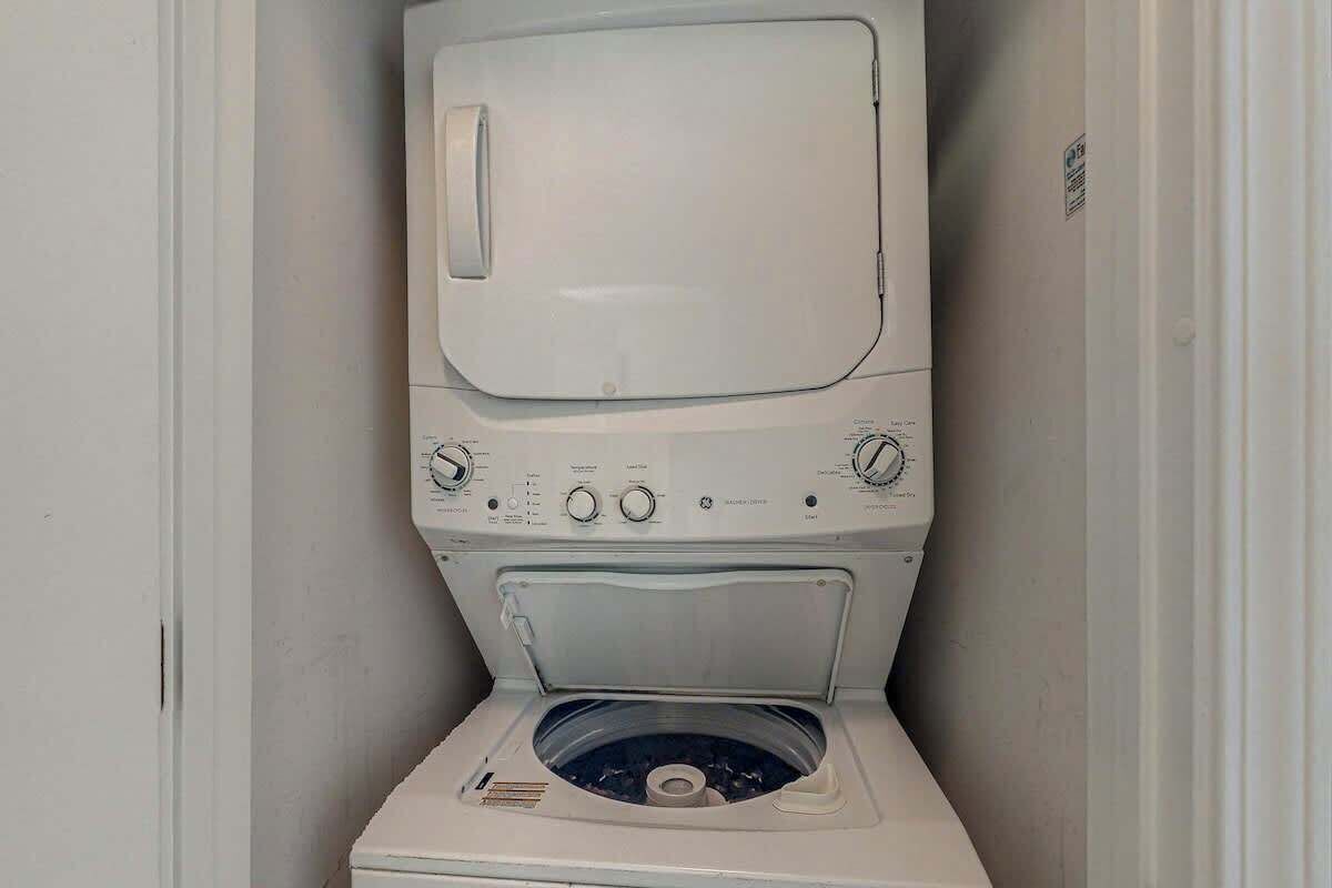Un appareil compact, blanc, comprenant une machine à laver et un sèche-linge, conçu pour être fixé au mur, doté de boutons de commande et d’une porte transparente.