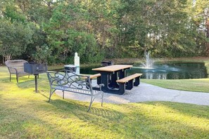 Ein Sitzbereich im Freien mit Grill, Tisch und Bänken in der Nähe eines Teichs.