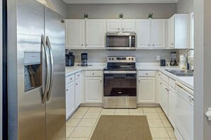 Una cocina moderna con electrodomésticos de acero inoxidable, armarios blancos y piso de baldosas.
