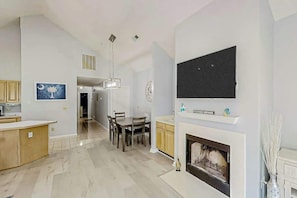 A spacious living area with a fireplace, a dining table, and a kitchen area with wooden cabinets. - Tidewater Dream Retreat (North Myrtle Beach)