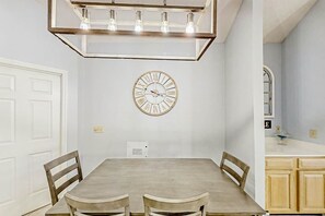 A dining area with a rectangular table, four chairs, a wall clock, and a pendant light fixture. - Tidewater Dream Retreat (North Myrtle Beach)