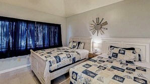 A bedroom with two beds, a large window with curtains, a wall clock, and a bedside table with a lamp. - Tidewater Dream Retreat (North Myrtle Beach)