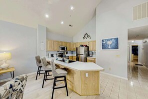 A modern kitchen with a central island, wooden cabinets, stainless steel appliances, and a dining area with chairs. - Tidewater Dream Retreat (North Myrtle Beach)