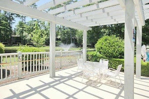 A covered patio area with white metal chairs and tables, a white fence, and a fountain. - Tidewater Dream Retreat (North Myrtle Beach)
