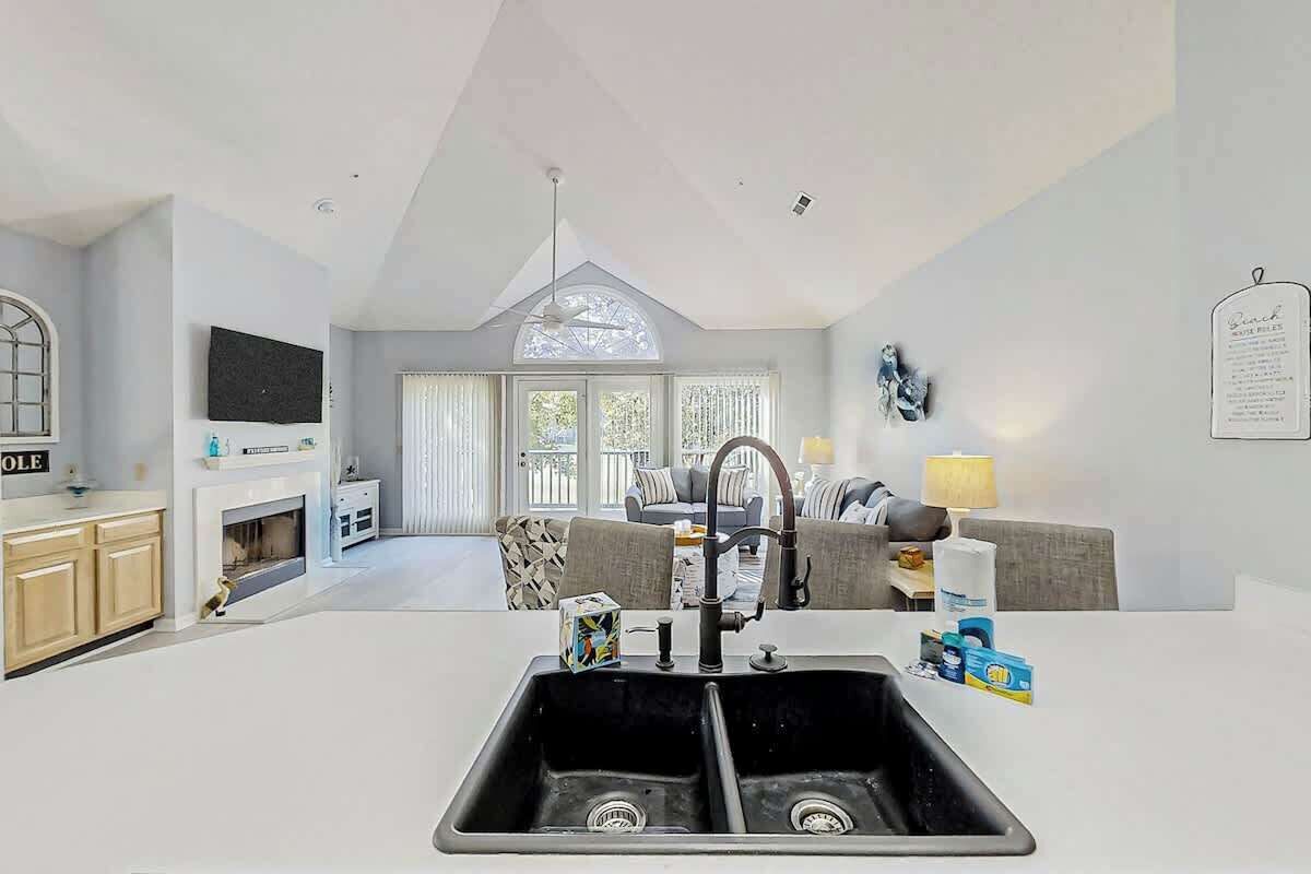 A modern kitchen with a double sink, a dining area with a sofa and table, and a large window providing natural light.