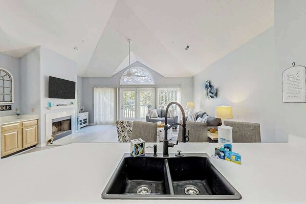 A modern kitchen with a double sink, a dining area with a sofa and table, and a large window providing natural light. - Tidewater Dream Retreat (North Myrtle Beach)