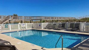 Piscina azul límpida com deck de madeira e espreguiçadeiras.