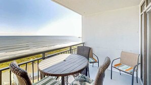 Uma varanda com vista para o oceano, uma mesa redonda, cadeiras de vime e um banco estofado.