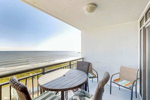 Ein Balkon mit Meerblick, ein runder Tisch, Korbmöbelstühle und eine gepolsterte Bank.