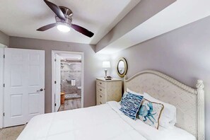 Ein Schlafzimmer mit Bett, Deckenventilator, Nachttisch, Spiegel und einer Tür zu einem Badezimmer.