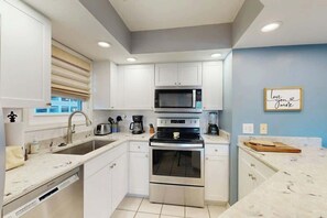 A modern kitchen with white cabinetry, stainless steel appliances, and a blue accent wall. - Shorehaven II Unit - 2C (North Myrtle Beach)