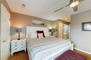 A bedroom with a bed, nightstands, a lamp, a bench, and a door. - Shorehaven II Unit - 2C (North Myrtle Beach)