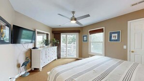 Een slaapkamer met een bed, plafondventilator, dressoir, televisie en een balkondeur.