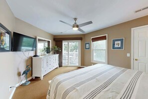 A bedroom with a bed, ceiling fan, dresser, TV, and a balcony door. - Shorehaven II Unit - 2C (North Myrtle Beach)