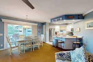 A modern kitchen with a central island, a dining area with white chairs, and a bar area labeled 'TIKI BAR'. - Shorehaven II Unit - 2C (North Myrtle Beach)