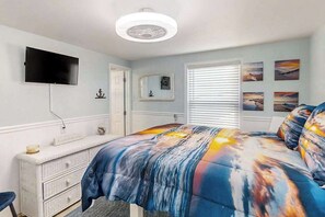 Une chambre à coucher comprenant un lit, une commode, un téléviseur fixé au mur et une fenêtre avec des stores.