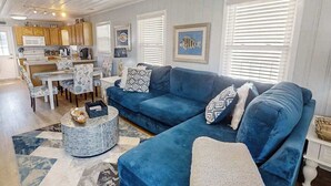 Een woonkamer met een blauwe bank, een eettafel met stoelen, en een keuken met houten kasten.