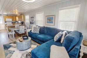 Ein Wohnzimmer mit blauem Sofa, einem Esstisch mit Stühlen und einer Küchenzeile mit Holzausbau.