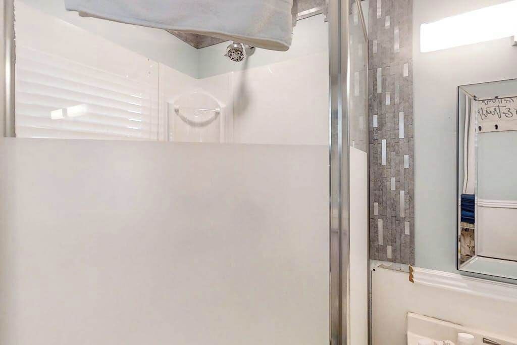 Een badkamer met een glazen douchecabine, een witte badkuip en een betegelde wand met een spiegel.