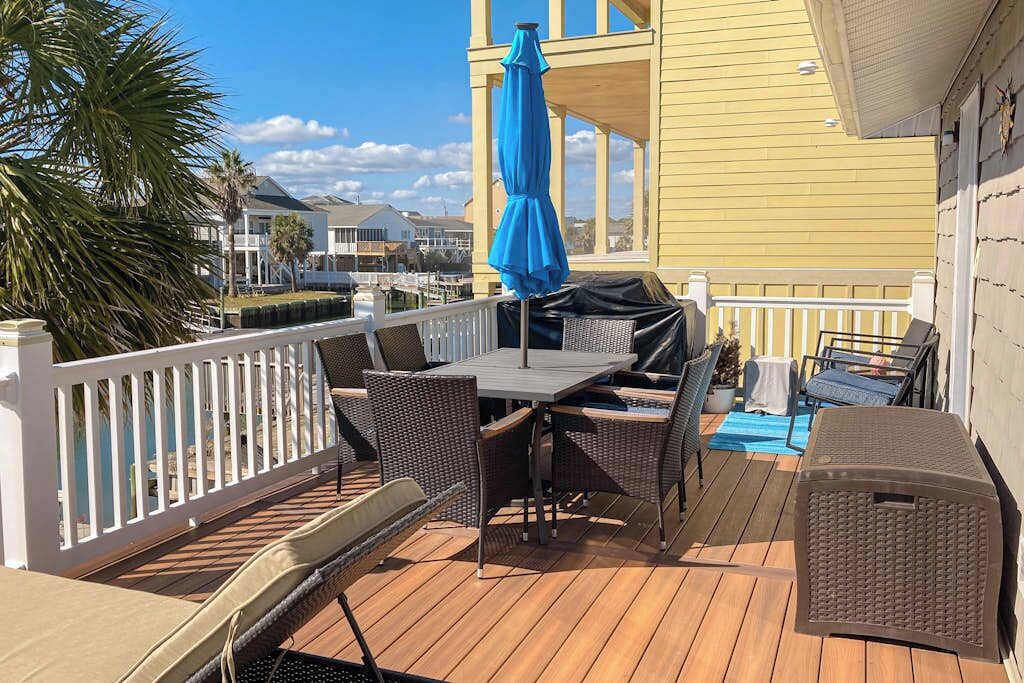 An outdoor deck with a table and chairs, a blue umbrella, and a view of the marina.