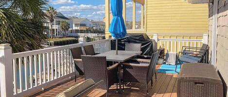An outdoor deck with a table and chairs, a blue umbrella, and a view of the marina.