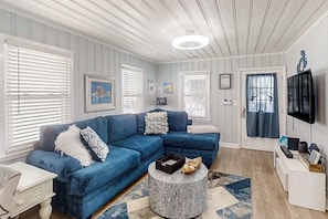 Ein Wohnzimmer mit einem blauen Ecksofa, einem runden Beistelltisch und einem flachbildfernseher an der Wand.