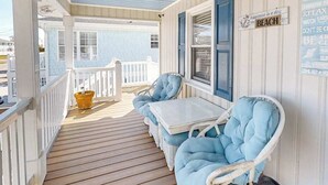 Een overdekt terras met een witte balustrade, een klein tafeltje en twee blauwe fauteuils met kussens.