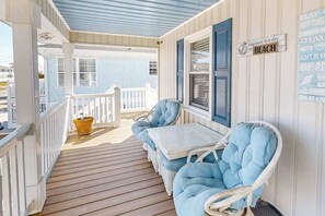 Eine überdachte Veranda mit weißer Geländer, einem kleinen Tisch und zwei blauen Polsterstühlen.
