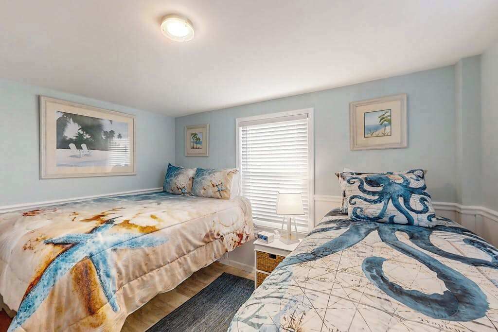 A bedroom with two beds, a window with blinds, and wall art.